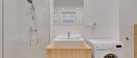 A modern bathroom with a glass-enclosed shower, a sink, and a built-in washing machine.