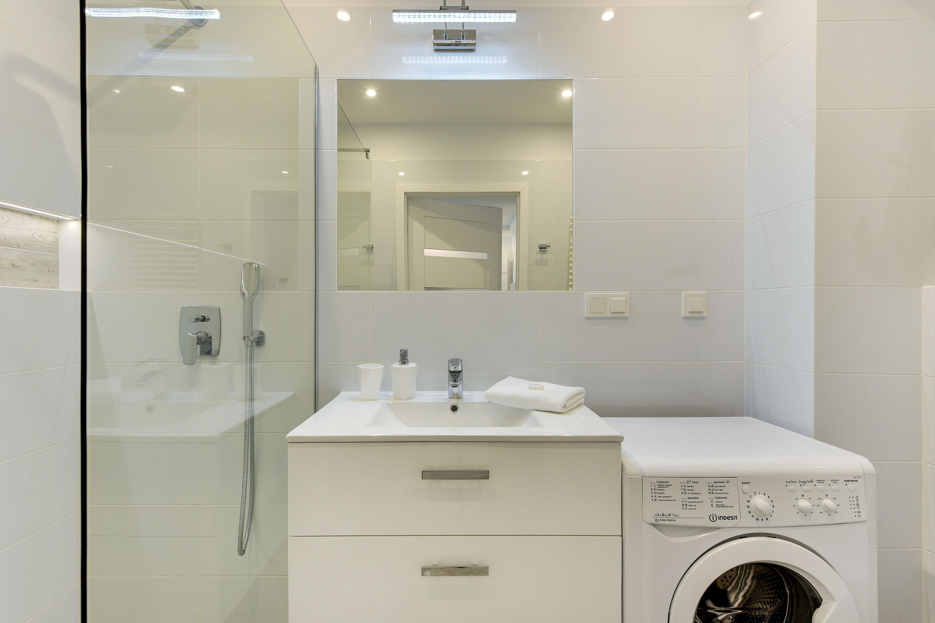 A modern bathroom with a glass shower enclosure, a sink with a mirror, and a built-in washing machine.