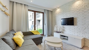 Een moderne woonkamer met een grijze bank, gele kussens, een witte tv-meubel en een klein tafeltje.