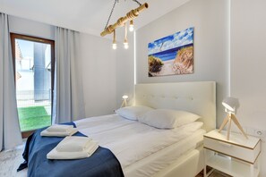 Quarto de hotel com cama, mesas de cabeceira, um quadro de uma praia e vista para o exterior.