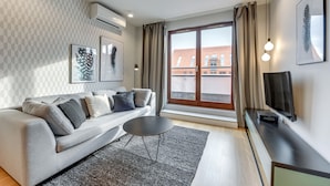 Een moderne woonkamer met een grijze bank, een kleine ronde tafel en een tv op een dressoir.