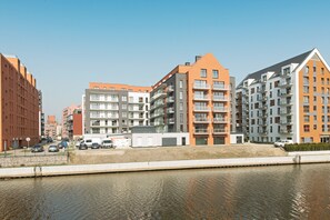 A modern apartment building with multiple balconies, a river in the foreground, and a clear sky. - Apartinfo Aura Island Apartments (Gdansk)