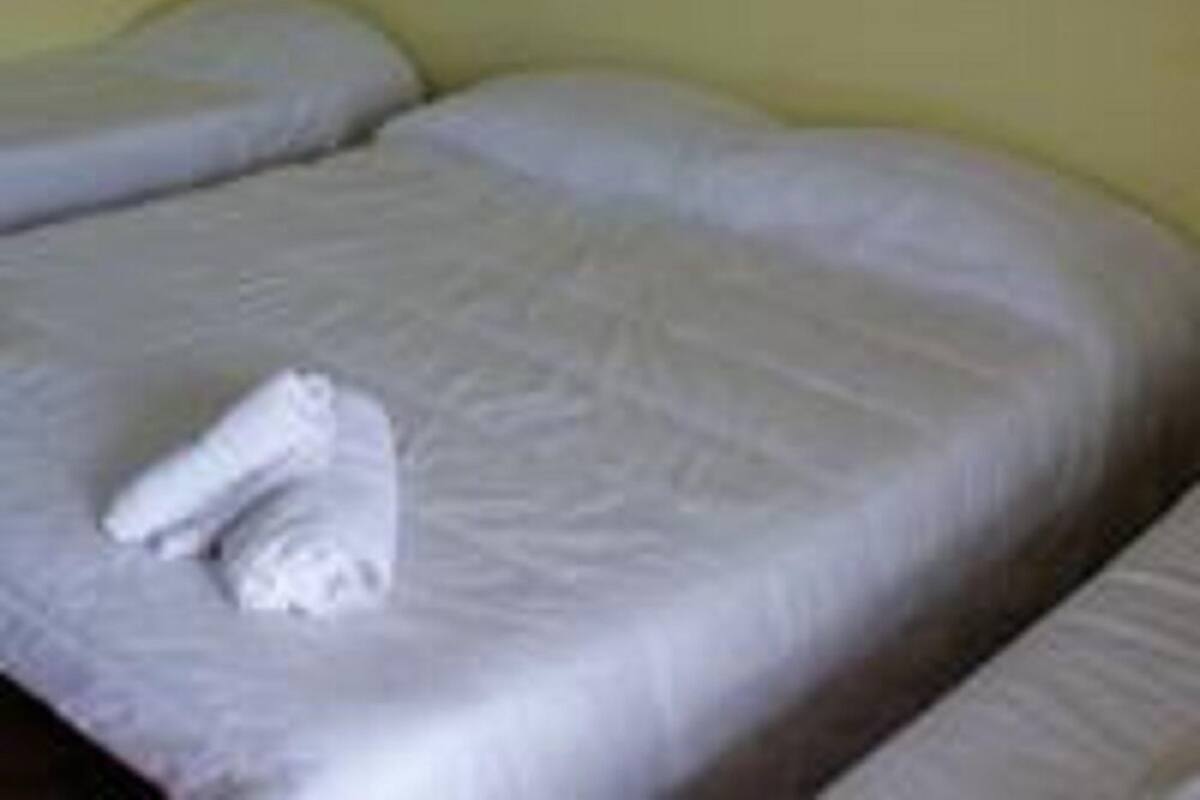 A single bed with a white blanket and a folded towel on it.