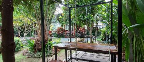 Un columpio de madera con estructura metálica, rodeado de abundante vegetación y un jardín.