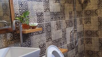 Un baño con inodoro y lavamanos blancos, ducha con cabezal de ducha manual y azulejos decorativos.
