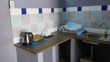 Una cocina con mostrador, hervidor, cesta de aperitivos, vaso y pileta.