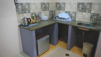 A compact kitchen with a refrigerator, sink, and tiled backsplash.