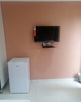Quarto com televisão fixada na parede, um frigorífico branco e chão em azulejos.