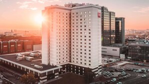 A high-rise hotel with a prominent 'ibis HOTEL' sign, multiple floors, and a parking area in front. - ibis Poznan Centrum (Poznan)