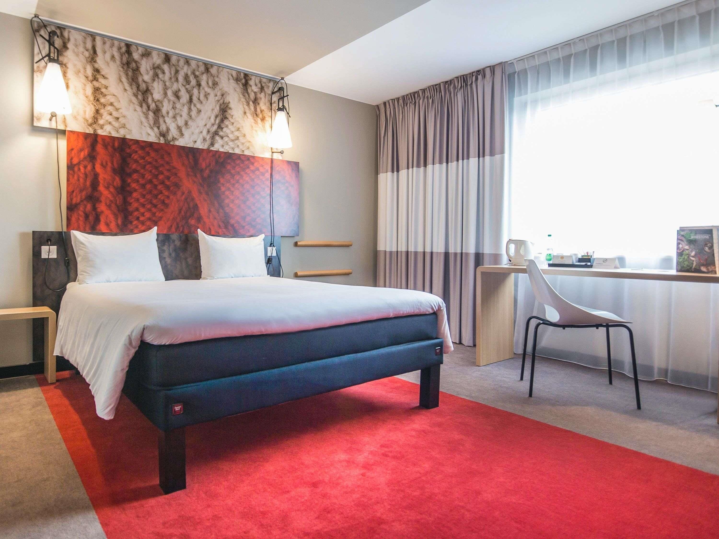 Ett hotellrum med en stor säng, ett skrivbord, en stol och utsikt över omgivningarna.