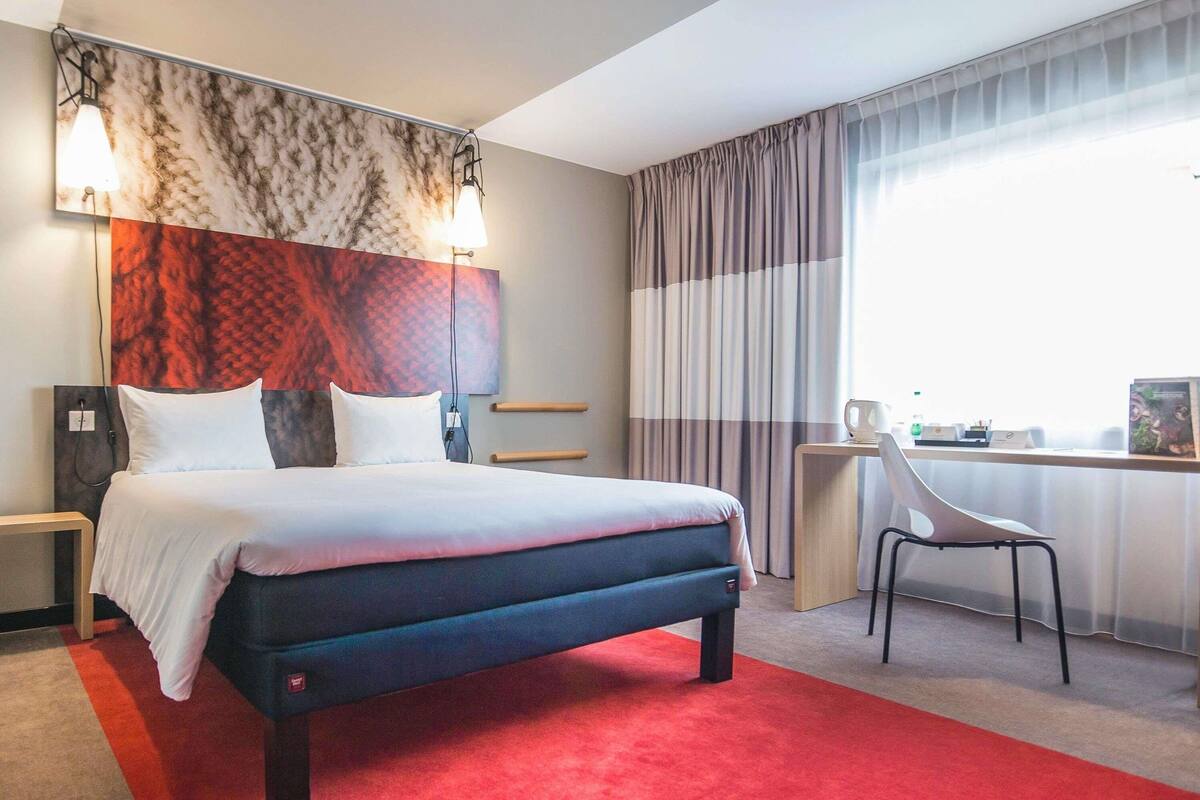 A hotel room with a large bed, a desk, a chair, and a view of the outdoors.