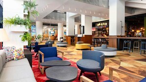 A modern lobby with seating areas, a bar, and a television screen. - ibis Poznan Centrum (Poznan)