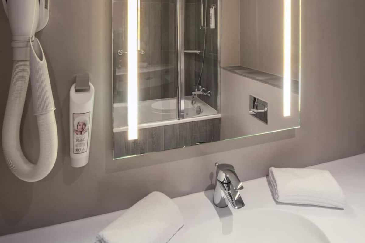 A modern bathroom with a large mirror, a hairdryer, a towel rack, and a sink.