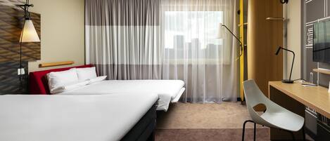 Habitación de hotel con cama, escritorio, silla, televisor y ventana con cortinas traslúcidas.