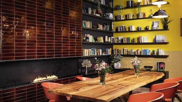 A modern interior with a wooden table, red chairs, bookshelves, and a fireplace.
