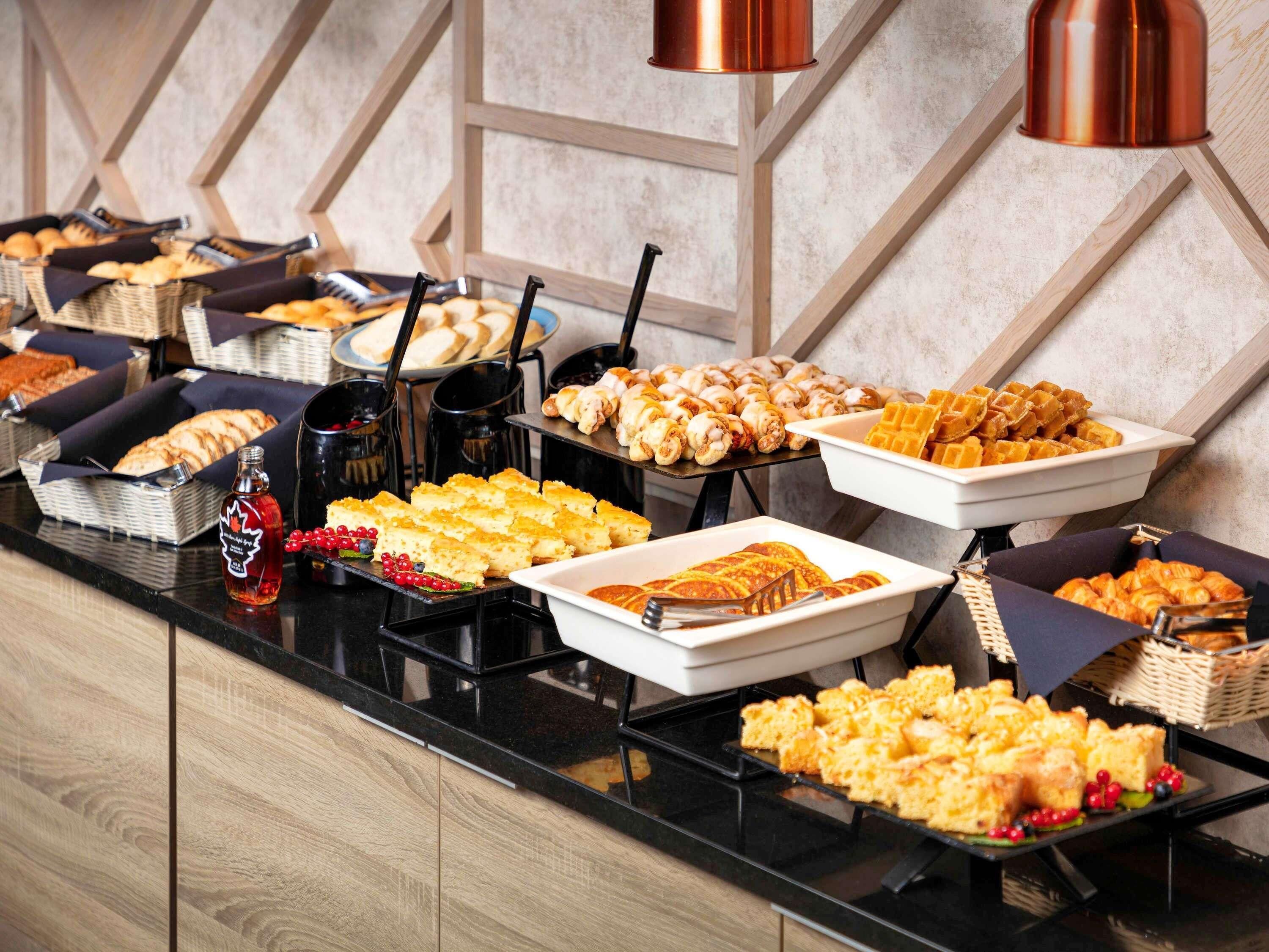 Ein reichhaltiges Buffet mit verschiedenen Speisen, darunter Gebäck, Waffeln und eine Flasche Sirup.