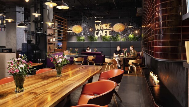 A modern cafe interior with wooden tables, orange chairs, and pendant lighting. - ibis Poznan Centrum (Poznan)
