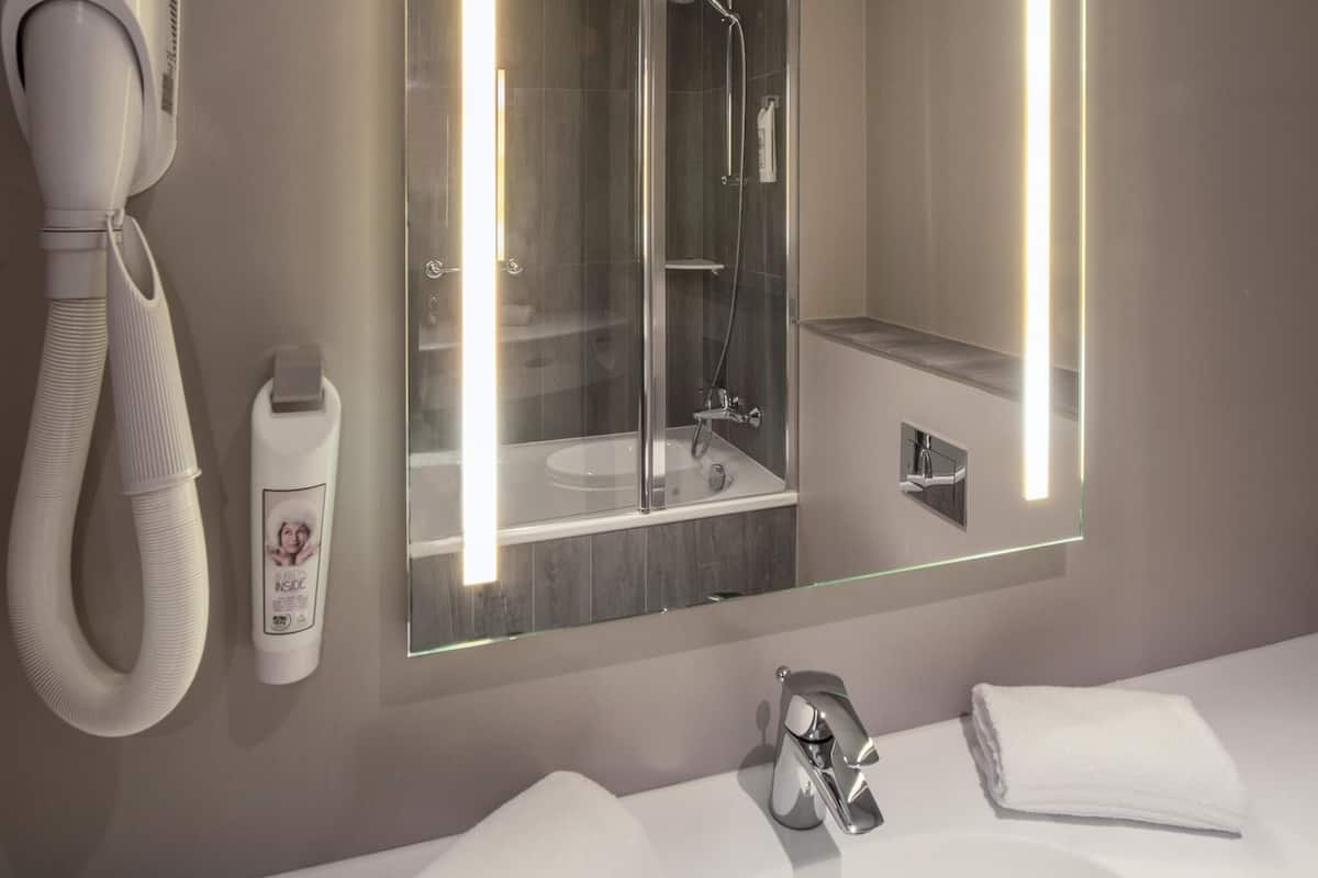 A modern bathroom with a glass-enclosed shower, a white sink, and a hairdryer mounted on the wall.