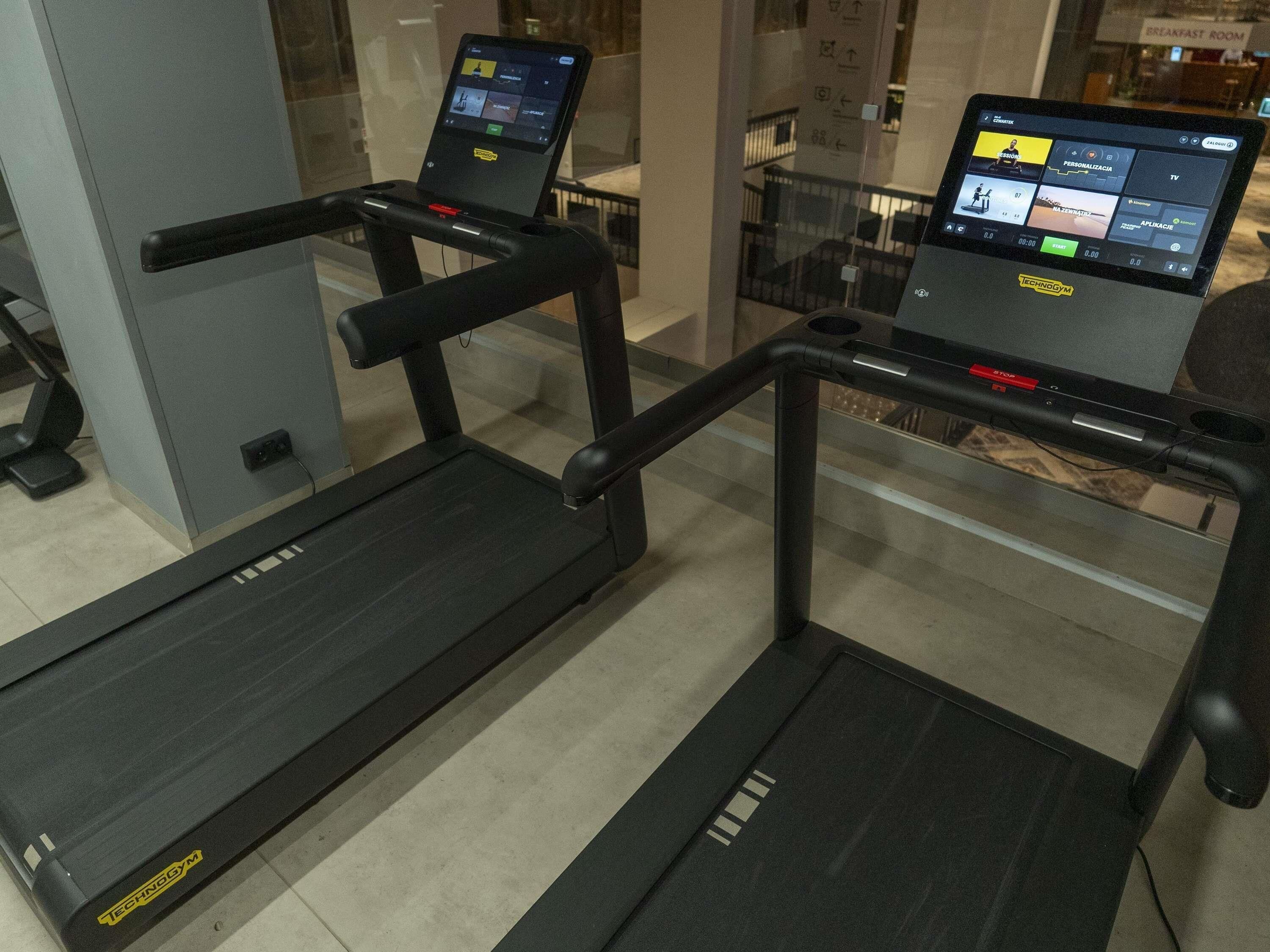 A treadmill with a digital display and a control panel, located in a modern indoor setting with glass partitions.
