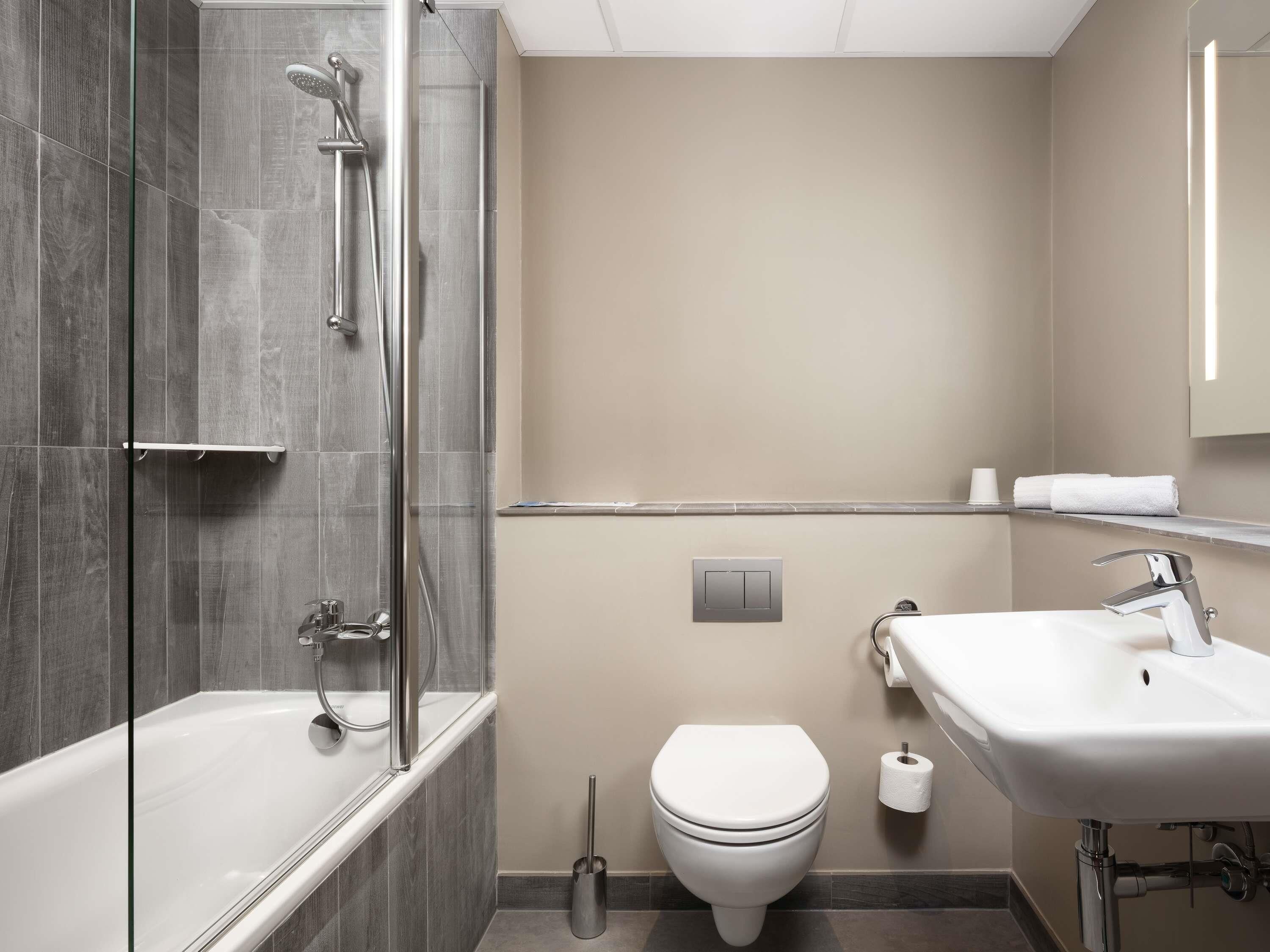 A modern bathroom with a glass-enclosed shower, a white toilet, and a sink with a mirror.