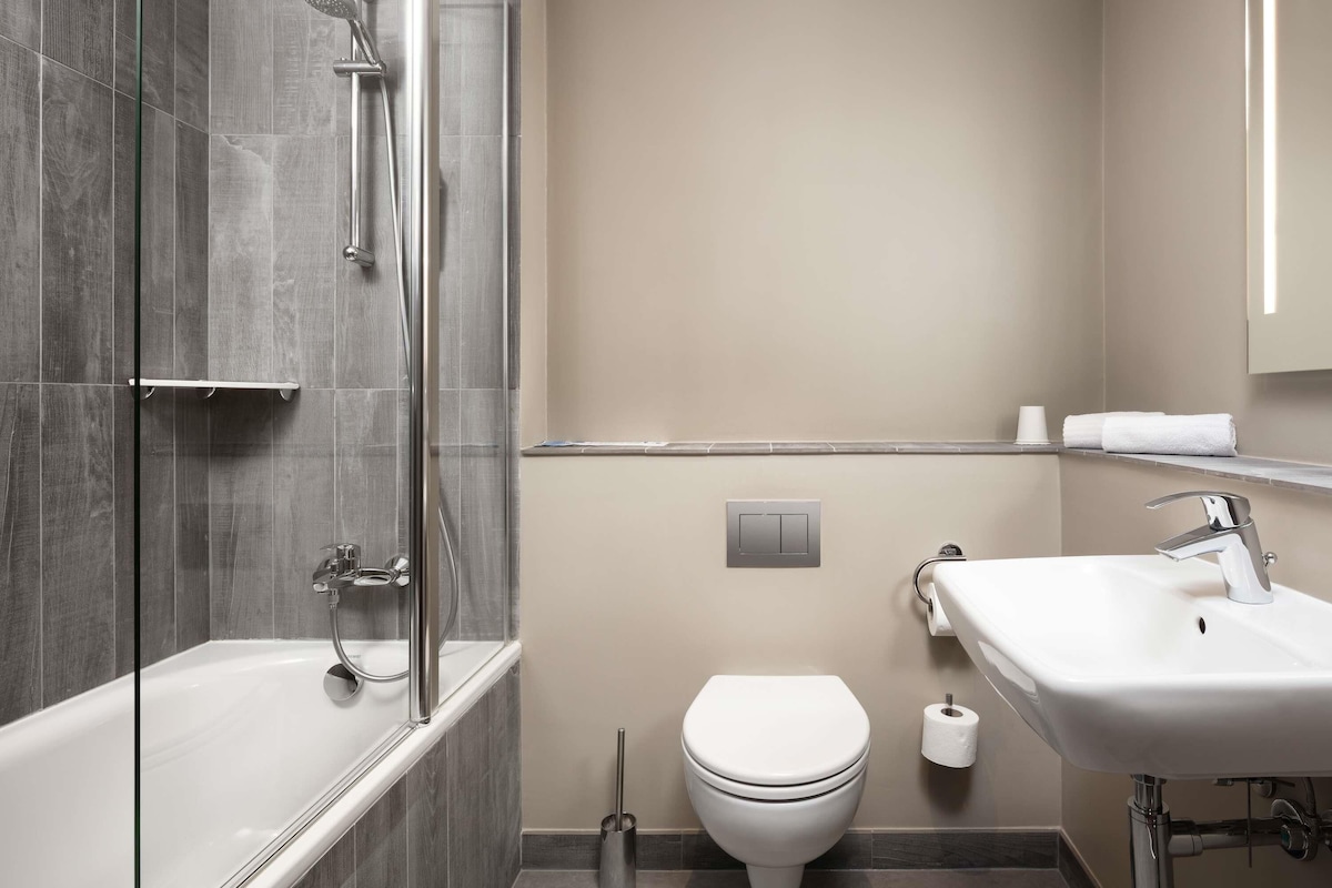 A modern bathroom with a glass-enclosed shower, a white toilet, and a sink with a mirror.