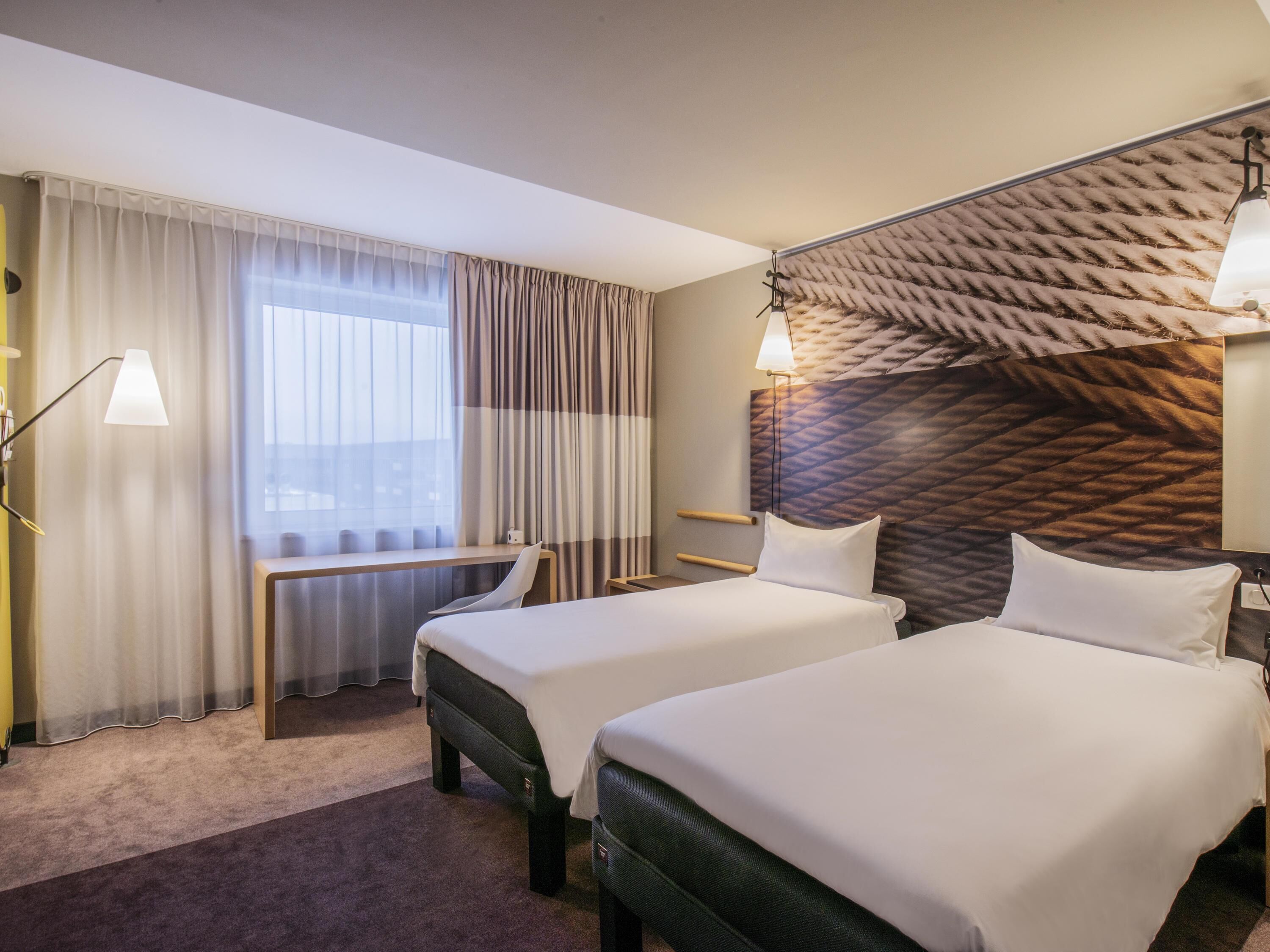 Une chambre d’hôtel avec deux lits, un bureau, une chaise, une lampe et une vue sur la ville.