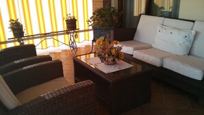 A cozy outdoor seating area with wicker furniture and a white sofa, featuring a table with a floral centerpiece. - Marinella B (Cornale e Bastida)