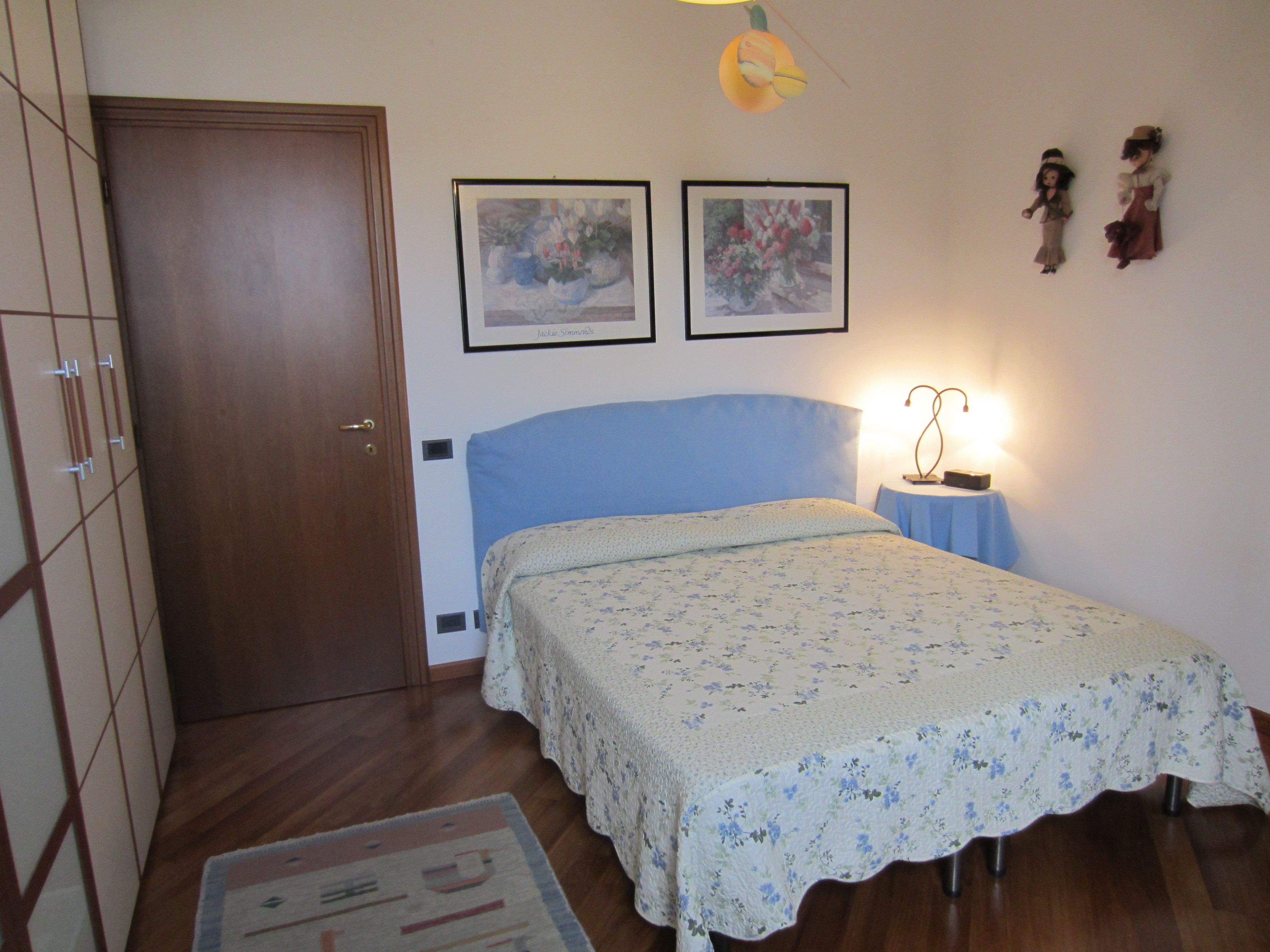 A bedroom with a bed, a nightstand, a lamp, and two framed pictures on the wall.