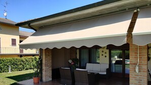 A covered outdoor seating area with a brick wall, a sofa, and a table. - Marinella B (Cornale e Bastida)