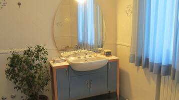 A bathroom with a sink, mirror, and potted plant.