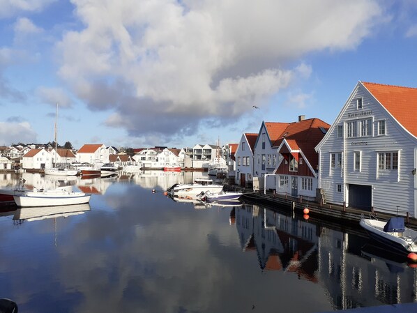 A harbor with white buildings with red roofs, boats docked, and calm water reflecting the buildings. - Skudenes Camping (Karmoy)