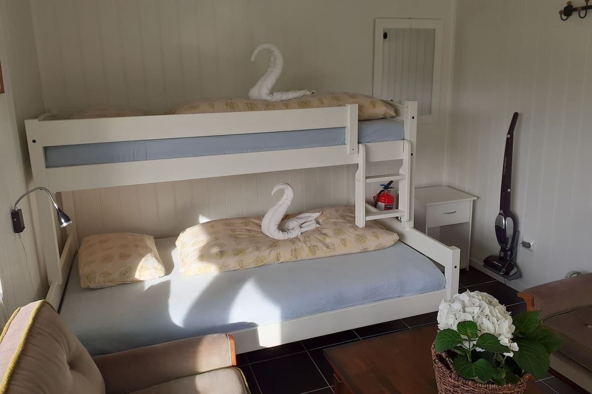 A bunk bed with two swan-shaped pillows, a bedside table with a fire extinguisher, a lamp, and a vacuum cleaner.