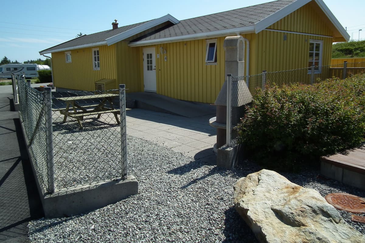 A yellow building with a grey roof, a small porch, and a chain-link fence.