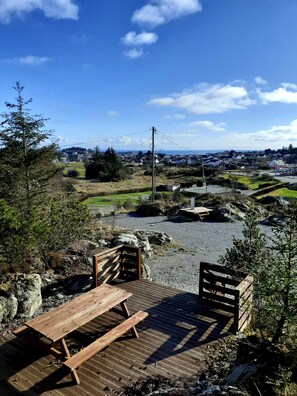 A wooden deck with picnic tables overlooking a rural landscape with houses and a gas station in the distance. - Skudenes Camping (Karmoy)