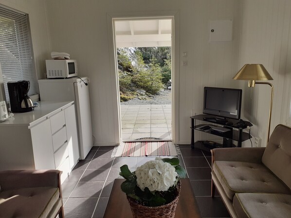 A compact living space with a kitchenette, a television, a sofa, and a view of a garden through a door. - Skudenes Camping (Karmoy)
