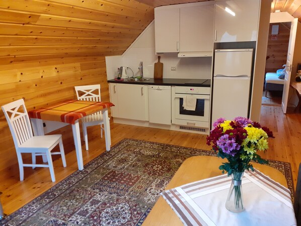 A compact kitchen with white cabinets, a built-in oven, and a refrigerator. There's a dining area with a table and chairs, and a decorative rug on the floor. - Skudenes Camping (Karmoy)