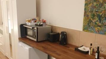 Cocina compacta con microondas, tostadora y cafetera sobre una encimera de madera. Se observa un refrigerador y un pequeño armario debajo. Un cuadro adorna la pared sobre la encimera.