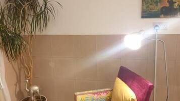 Una habitación pequeña con una silla, una planta en maceta, una lámpara de pie y un cartel en la pared.