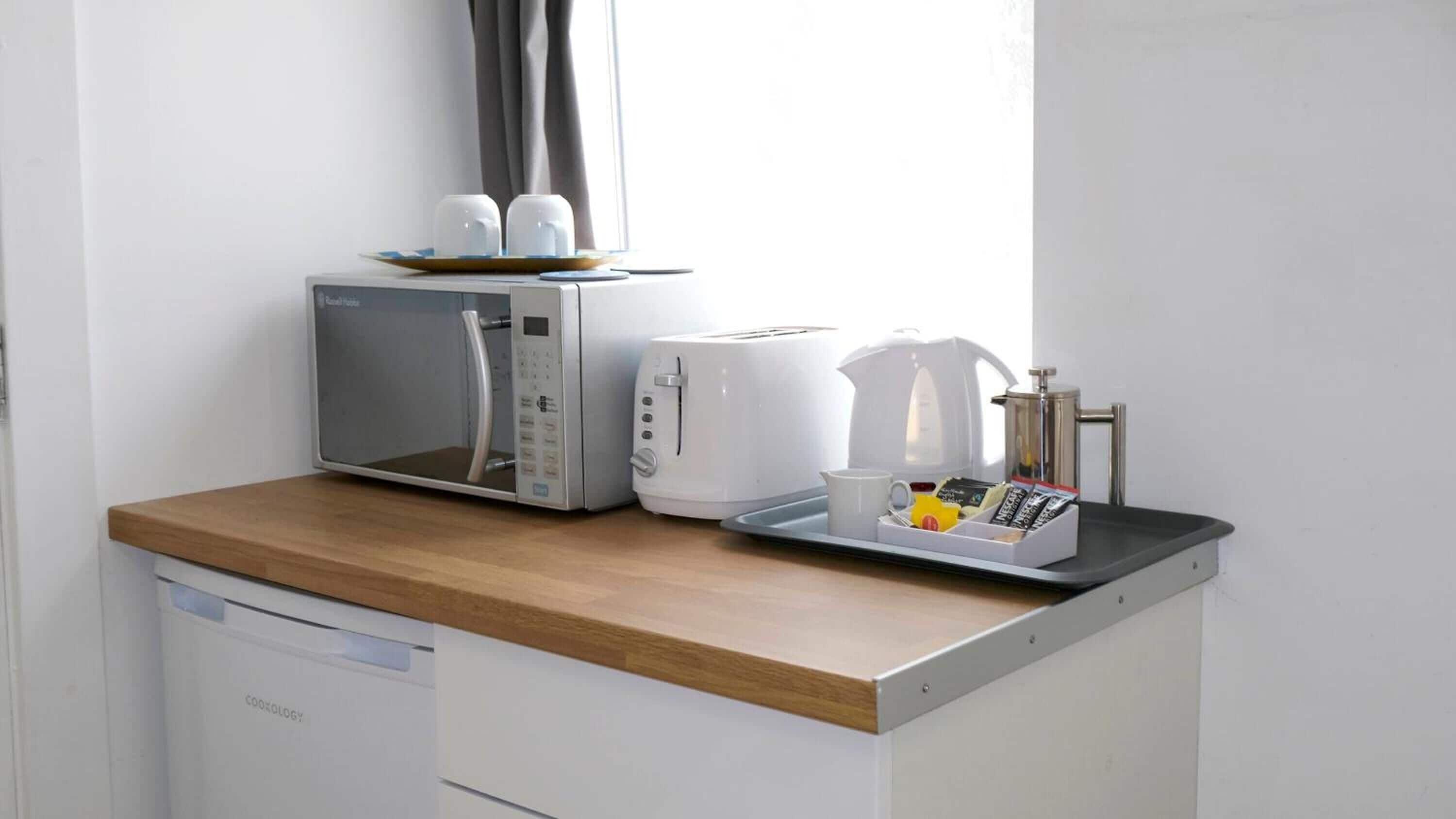 Una kitchenette con microondas, tostadora, hervidor y cafetera sobre una encimera de madera.