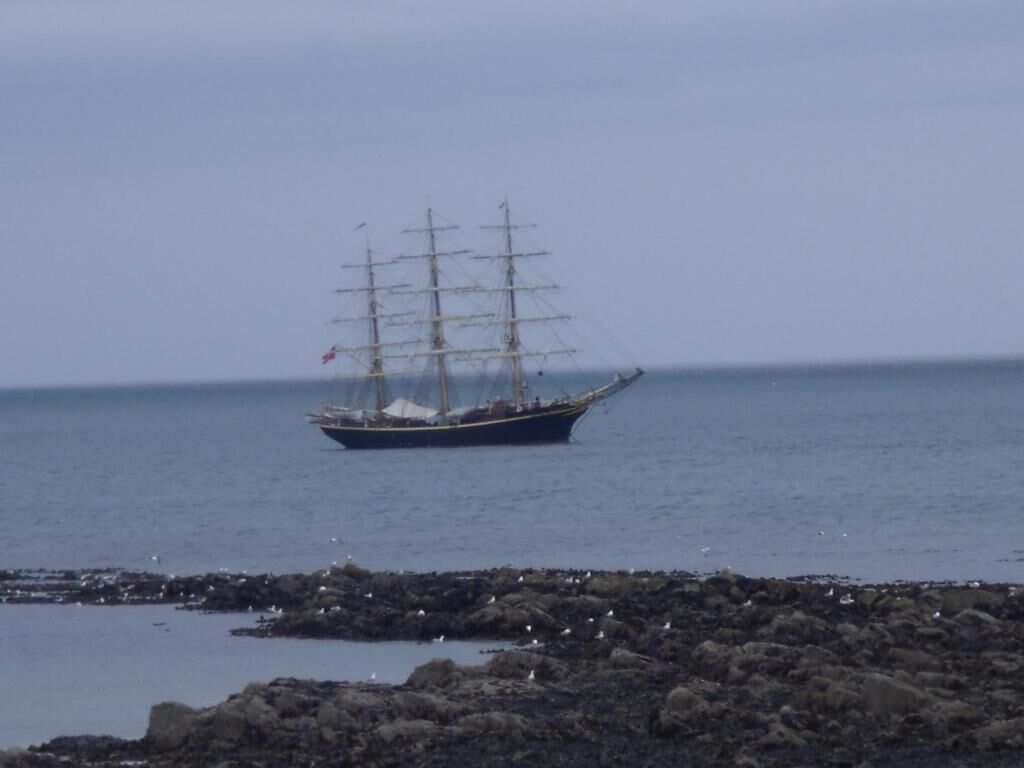 A sailing ship on calm waters near rocky shores.