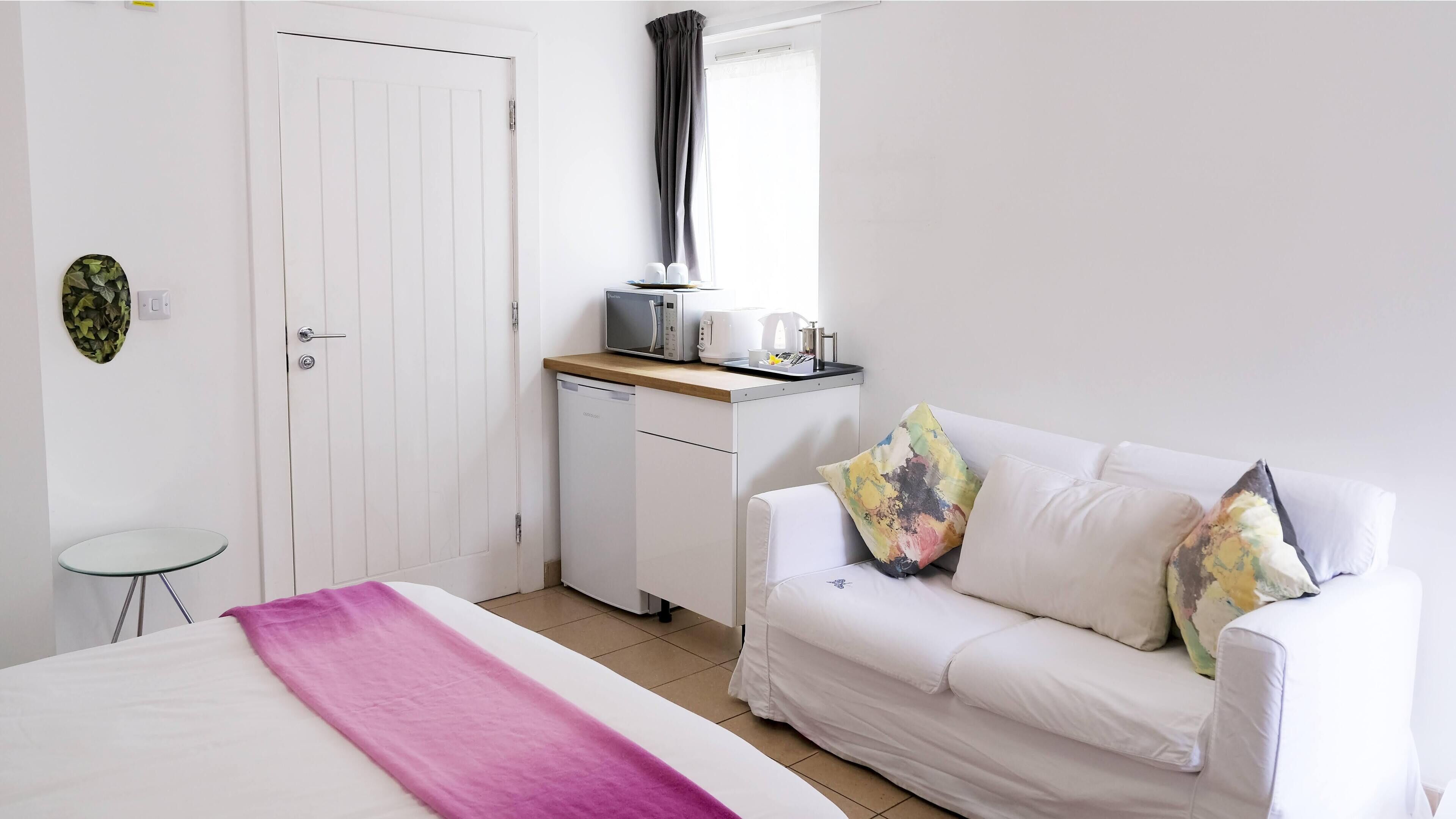 A bedroom with a bed, a white sofa, a small table, a microwave, and a coffee maker.