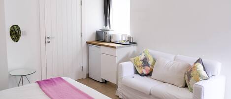 A bedroom with a bed, a white sofa, a small table, a microwave, and a coffee maker.