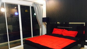 A modern bedroom with a black bed, red bedding, and a sliding glass door leading to an outdoor area. - Casa D Pool Huahin 1 (Hua Hin)