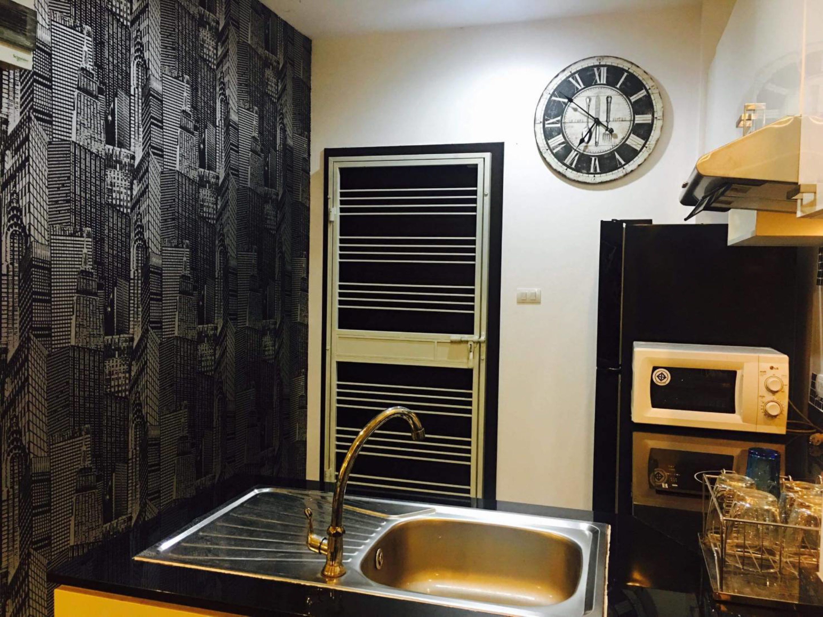 A compact kitchen with a sink, a clock, and a microwave.