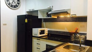 A compact kitchen with a black refrigerator, a microwave, a sink, and a clock on the wall. - Casa D Pool Huahin 1 (Hua Hin)