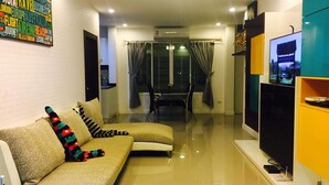 A modern living room with a sofa, a flat-screen TV, and a dining area with a table and chairs. - Casa D Pool Huahin 1 (Hua Hin)