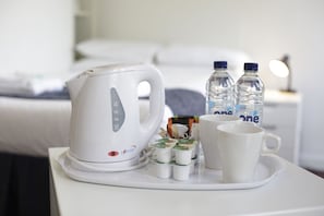A white kettle, two water bottles, and two white cups on a tray.