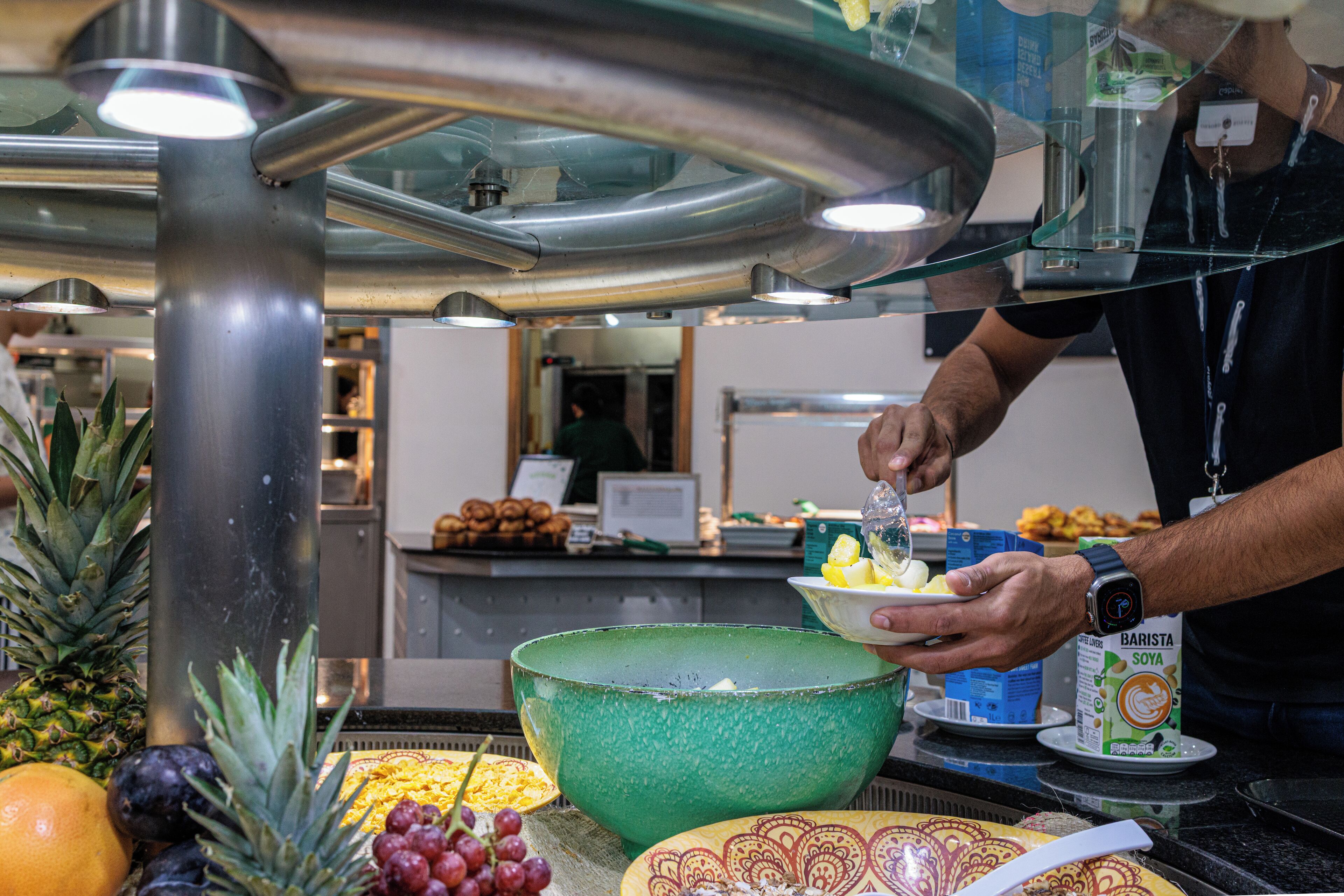 A buffet area with a large green bowl, a pineapple, and a plate with sliced fruit.