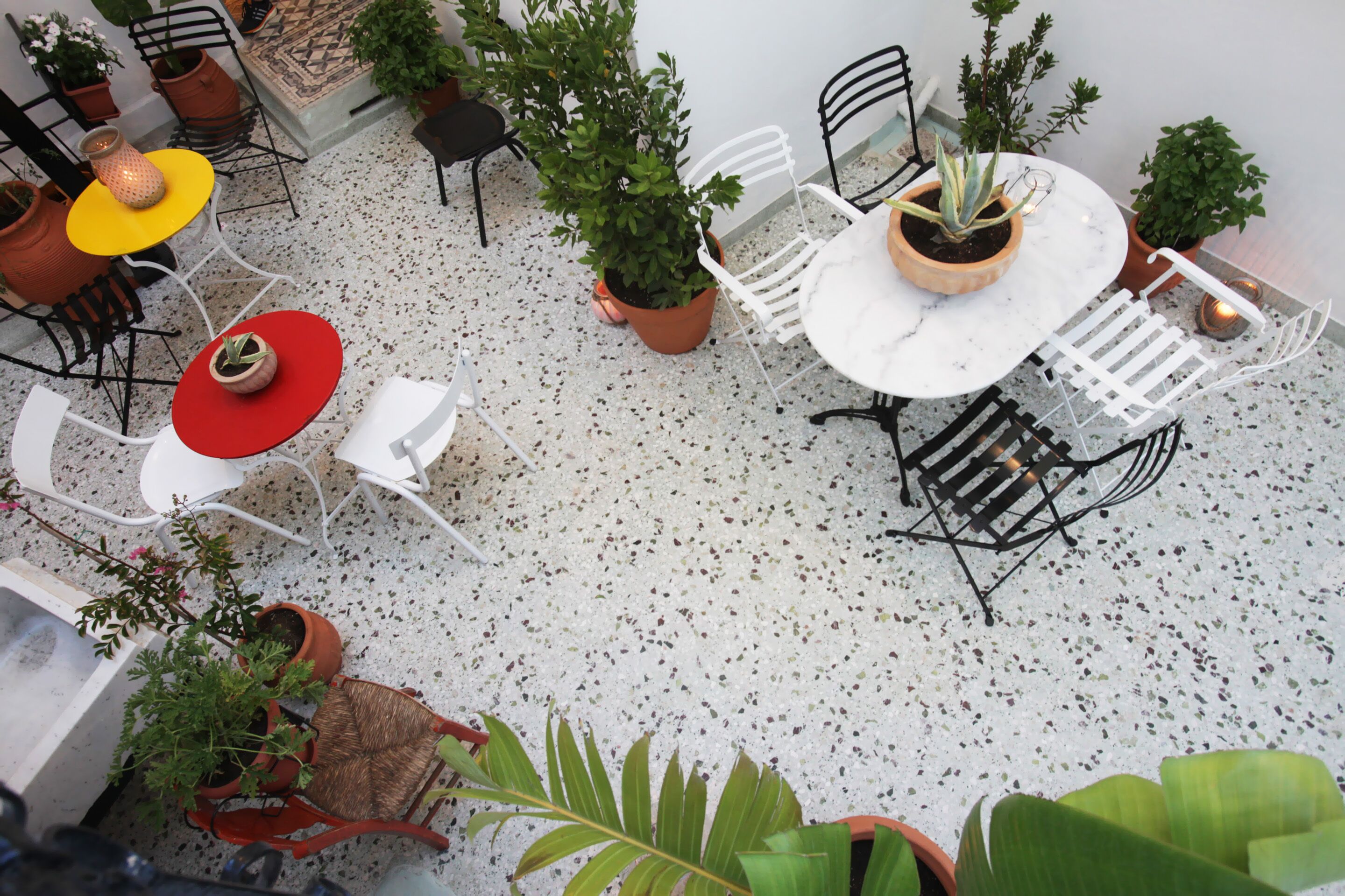 Eine Dachterrasse mit weißem Tisch und Stühlen, umgeben von Blumentöpfen und einer kleinen Sitzecke.