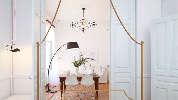 A bedroom with a canopy bed, a bedside table, a lamp, and a view of a dining area with a table and chairs. - Live in Athens, Thiseio Historic House (Athens)